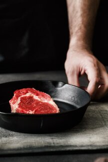 Ein Mann bereitet ein Steak in einer gusseisernen Pfanne zu.
