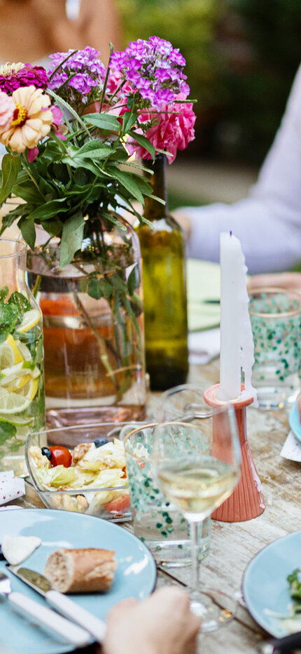 Eine Gruppe von Menschen genießt gemeinsam eine Mahlzeit im Freien an einem Tisch mit verschiedenen Gerichten.