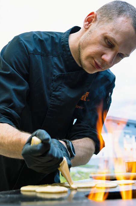 Ein Koch in schwarzer Uniform konzentriert sich in einer professionellen Küche voll und ganz auf die Dekoration eines Desserts.