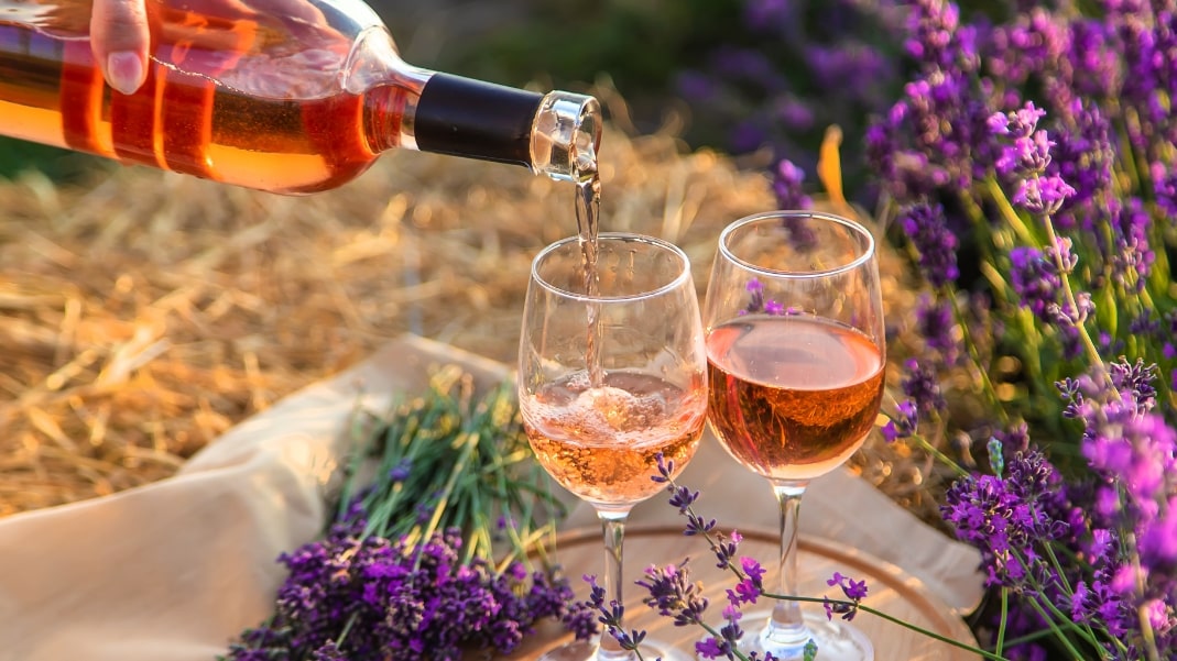 Zwei Gläser Wein werden in der Natur gegossen. Im Hintergrund sind Lavendelblüten.