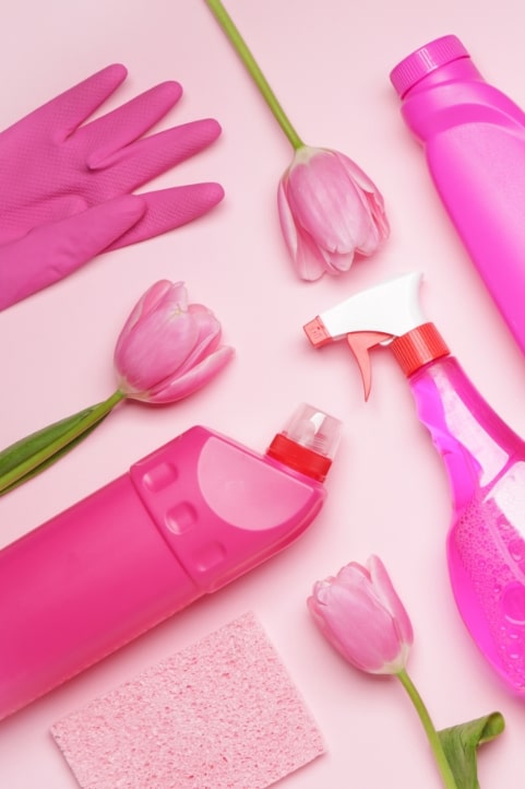 Rosa Putzmittel und Handschuhe auf rosa Hintergrund