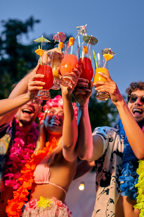 Eine Gruppe von Menschen in farbenfrohen Outfits und Sonnenbrillen hält bei einem sonnigen Open-Air-Festival verschiedene hawaiianische Blumenketten hoch.