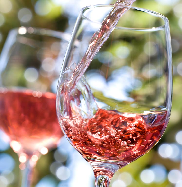 Ein Spritzer Rotwein wird eingefangen, wie er in ein Glas fällt, vor einem verschwommenen grünen Hintergrund.
