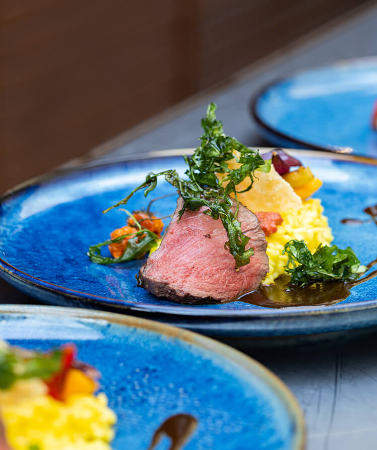 Ein Gourmetgericht mit Lachs und buntem Salat serviert auf einem blauen Teller, begleitet von einem Glas Weißwein.
