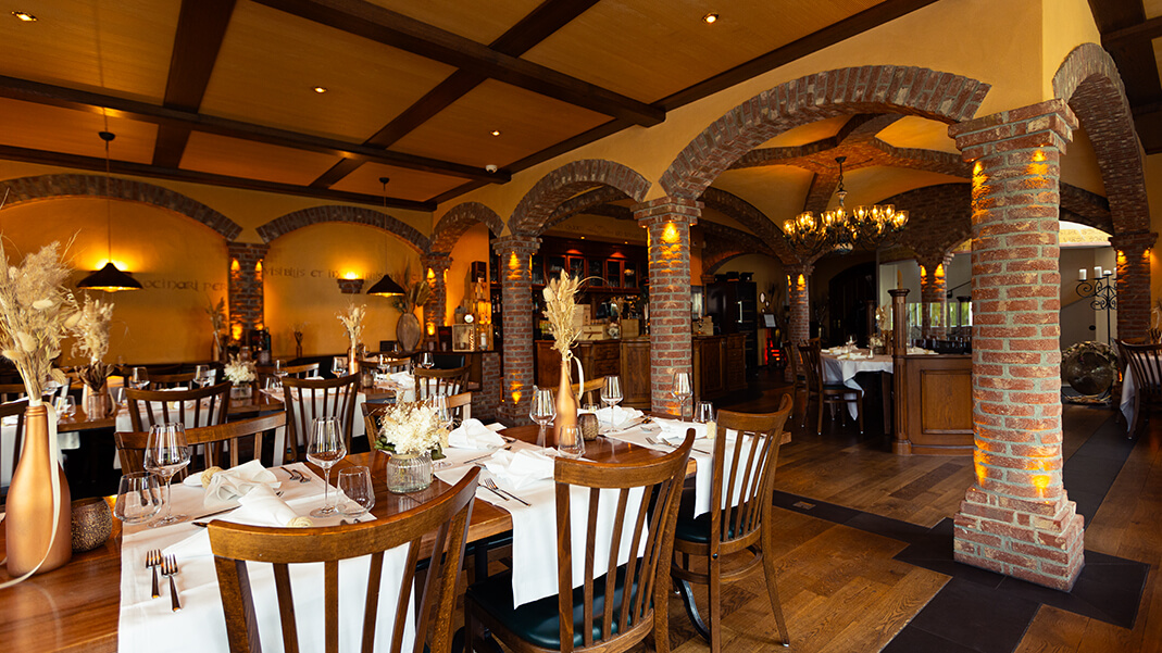Inneneinrichtung eines traditionellen Restaurants mit Holzmöbeln, verzierten Säulen und dekorierten Decken, die eine warme und einladende Atmosphäre schaffen.